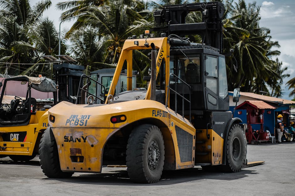 Heavy-duty forklift parked among tropical palm trees in a sunny storage area.